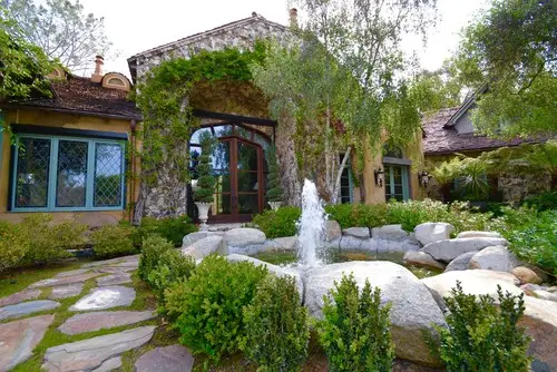 Naturalistic pool edged in boulders with a flagstone path leading to a stone house