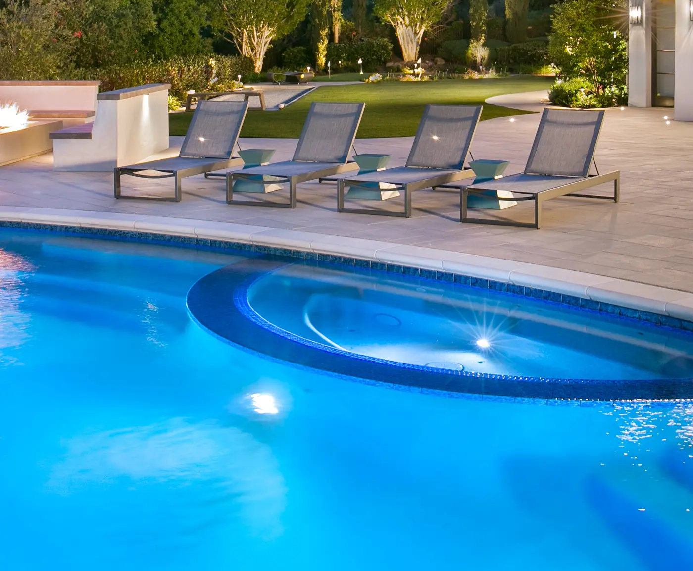 Pool at dusk with rounded precast concrete coping along its edge and four loungers on the deck